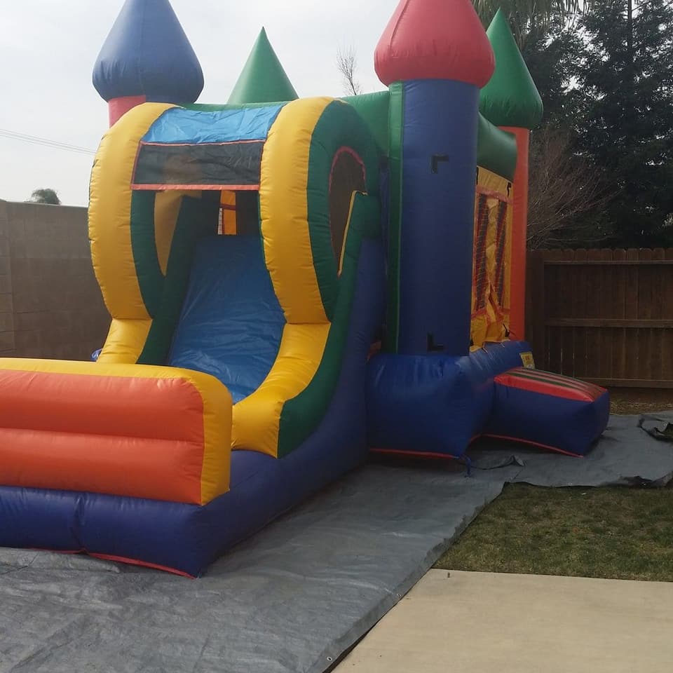 Combo bounce house with a slide, set up on a tarp in a fenced back yard